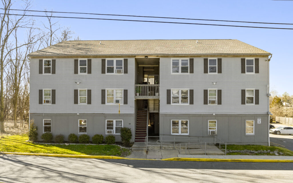 Exterior view of Robinson's three-story apartment building in Wilmington, DE, with grass, large trees, and resident parking.